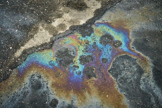 Gasoline or oil spill creates rainbow sheen on cracked asphalt surface
