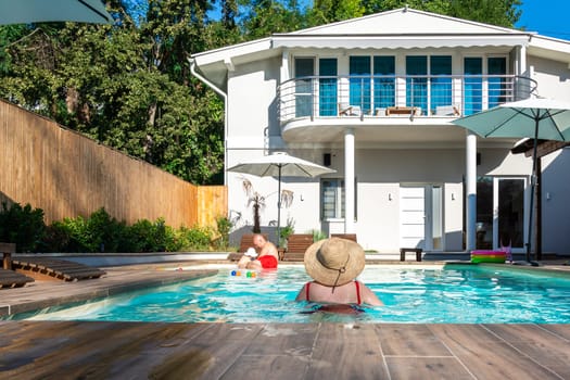 Parents with small child spending a relaxing day by the villa pool under the warm sun. Concept of family togetherness, happiness, and leisure during vacation