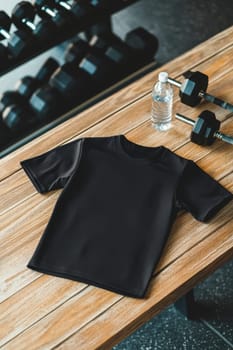 A sleek sports jersey mockup positioned on a wooden table, accented by gym essentials like dumbbells and a water bottle. the arrangement underscores fitness and modern style, ideal for branding, marketing, or athletic design concepts.
