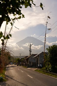 View of the volcano from the road decorated for the holiday in the village. Bamboo decorations along the road. A panorama of Mount Agung covered in clouds before sunset