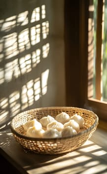 A woven basket filled with steamed buns by a sunlit window.