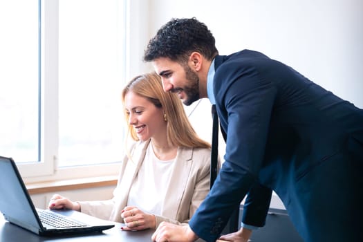 Professional man and woman working together on a laptop in a modern office. The woman points at the screen, explaining details while the man listens attentively.