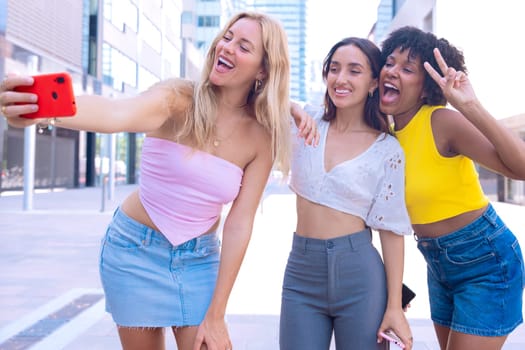 Three young women outdoors, smiling, and taking a playful selfie together. Perfect for concepts like friendship, happiness, social media, and outdoor lifestyle.