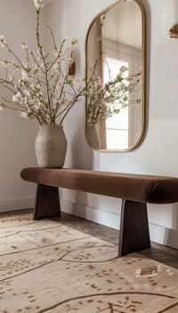 Elegant entryway setup with a mocha mousse bench and a gold-framed mirror, complemented by a patterned beige rug. a console table features a vase with fresh white flowers, creating a welcoming and stylish atmosphere.