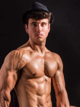 A muscular man showcases his well-defined physique while wearing a stylish hat. The portrait captures his confident expression against a dark background, emphasizing his strong build.