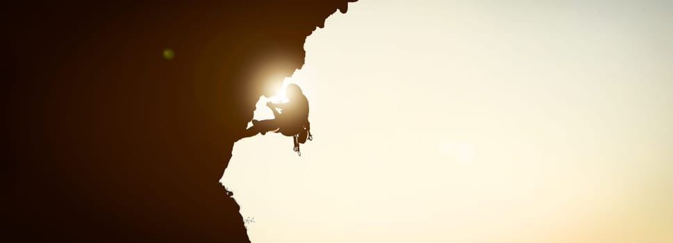 The black silhouette of a person climbs up the mountain against the background of the sky, leading an active lifestyle and involved in extreme sports, mountaineering and rock climbing.