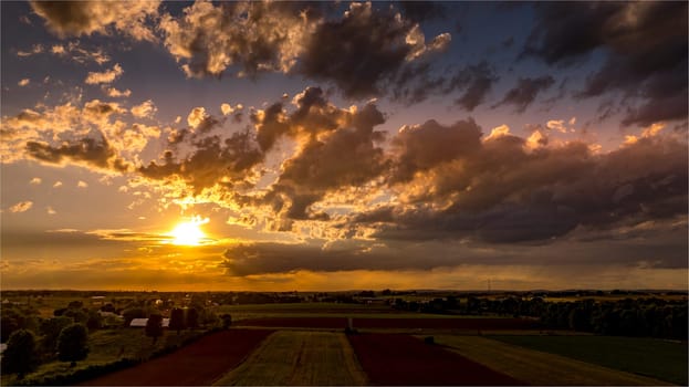 Golden sunlight breaks through clouds as the sun sets, creating a stunning display in the evening sky. The colorful clouds reflect warm tones, enhancing the serene atmosphere of dusk.