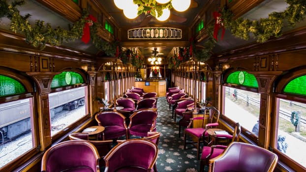 The interior of a vintage train car showcases plush seating and festive decorations, creating a warm atmosphere. Green and red accents enhance the cozy ambiance on a winter day.