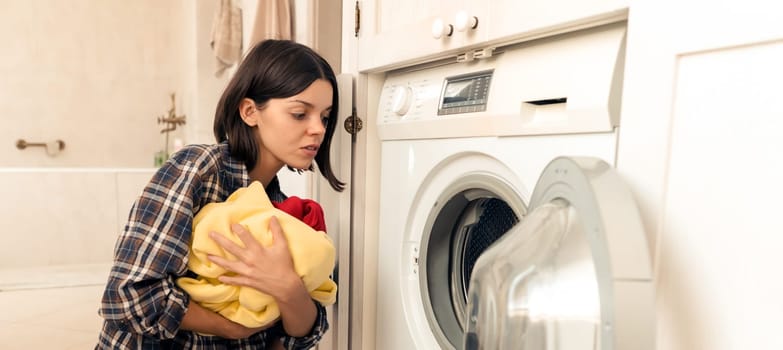 A young girl puts things in the washing machine, a woman sits on the floor of a cozy house and looks at clothes that need to be cleaned with washing powder.