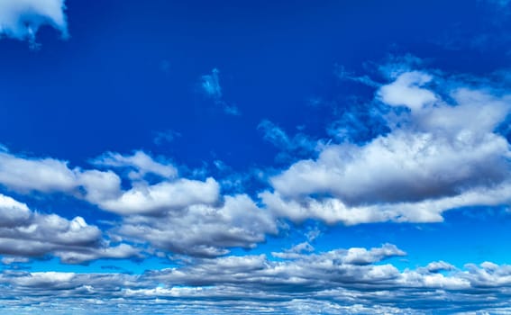 The sky stretches wide with vibrant blue, dotted by fluffy white clouds. The scene captures the essence of a bright, pleasant day, evoking a sense of calm and wonder in nature.