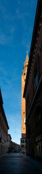 Cremona, Italy - November 27th 2024 Torrazzo of cremona, a medieval brick tower, dominates a narrow street with historic buildings under a clear blue sky in cremona, italy
