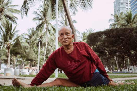 An elderly man of Asian descent is sitting on a twine under palm trees. The concept of wellness, motivation to take care of health. Nha Trang, Vietnam - July 21, 2024