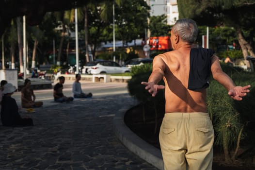 An elderly Asian man does physical exercises on the promenade near Nha Trang beach