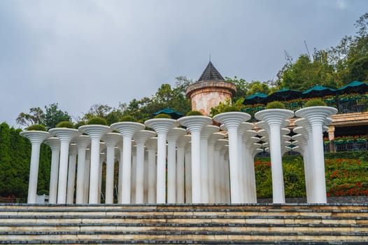 Many stone columns in the ancient style rise in a luxurious garden full of greenery. The columns add a classic architectural touch to the calm open space.