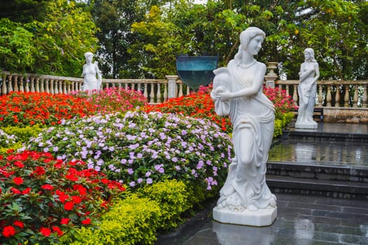 Sculptures of mythological goddesses with a vase in their hands made of white stone in a blooming garden