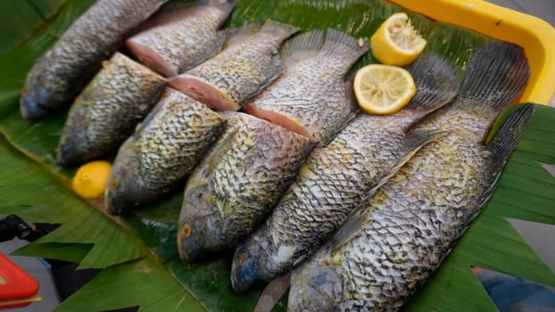 Whole range Guorami fish some kind of tilapia fish prepared for cooking or sale in supermarket are neatly arranged on banana leaves and garnished with lemons, this setup highlights seafood, tropical cuisine, and fresh ingredients for meals.