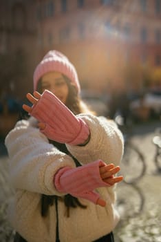 A cheerful young woman dressed in a cozy sweater and stylish pink mittens enjoys a sunny winter day outdoors