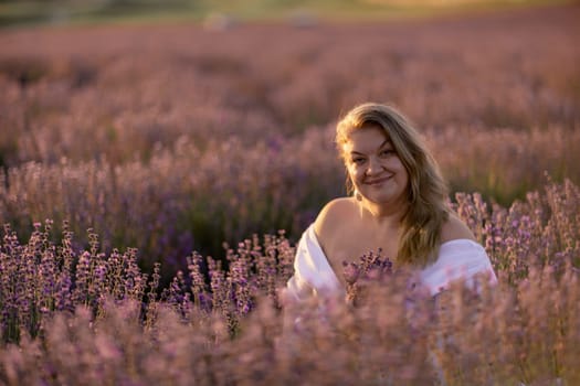 Woman poses in lavender field at sunset. Happy woman in white dress holds lavender bouquet. Aromatherapy concept, lavender oil, photo session in lavender.