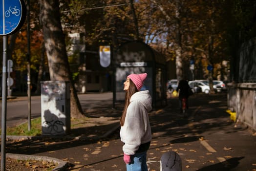 A woman on a serene path in an autumn park, in a cozy pink hat, gazes ahead, embracing the seasons beauty