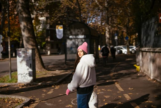 A young woman strolls through a picturesque autumn park, enveloped in delightful shades of cozy fashion attire