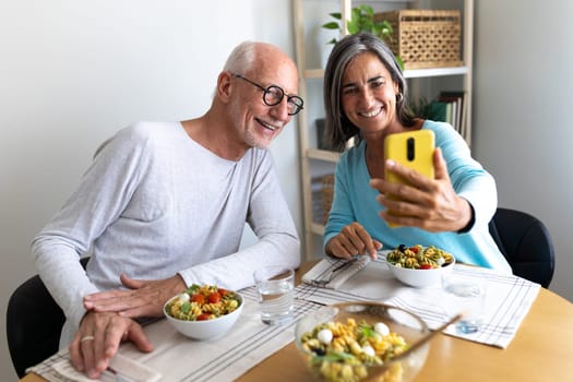 Happy mature married couple looking at phone while having lunch together at home. Lifestyle concept.