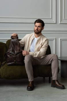 A man is comfortably seated on a sofa with a backpack resting beside him, creating a relaxed and casual atmosphere around him