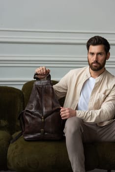 A man is comfortably seated on a sofa with a backpack resting beside him, creating a relaxed and casual atmosphere around him