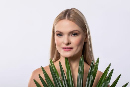 A calm young woman with long blonde hair gently holds a small plant, showcasing a fresh and natural vibe