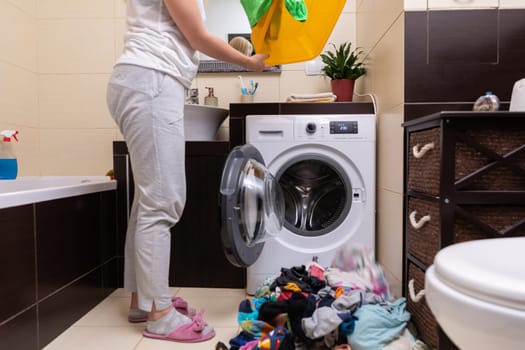 A person is organizing laundry in a modern bathroom with a washing machine and colorful clothes laid out