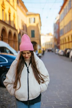A young woman, dressed warmly in her cozy attire, strolls leisurely through a charming urban street on a winter day