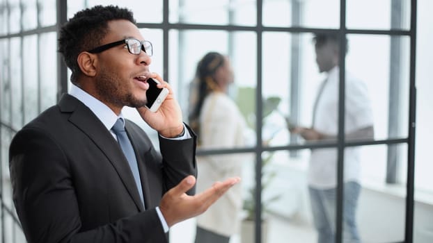 Close-up portrait of a smiling young african man talking on a mobile phone in the office against the background of colleagues