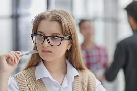 A beautiful young girl in the office works with documents, holds a pen in her hand and looks at the camera.