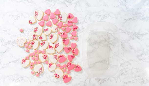 Flat lay. Storing heart-shaped sugar cookies with pink and white royal icing in a large plastic container.