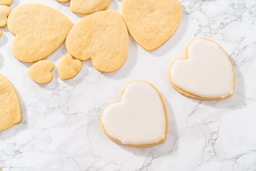 Decorating heart-shaped sugar cookies with pink and white royal icing for Valentine's Day.