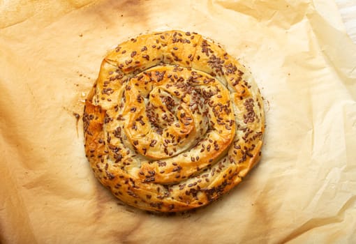 Freshly baked Burek made of filo dough with filling on baking paper background top view. Traditional savoury spiral pie of Balkans, Middle East and Central Asia.