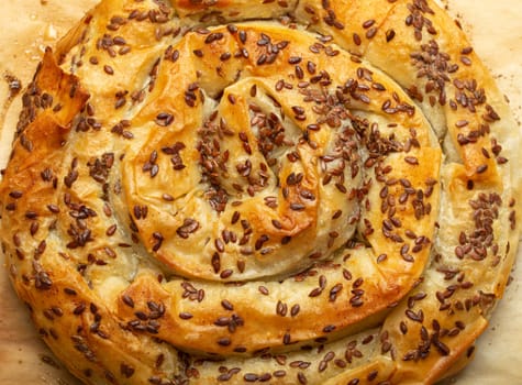 Freshly baked Burek made of filo dough with filling on baking paper background top view. Traditional savoury spiral pie of Balkans, Middle East and Central Asia.