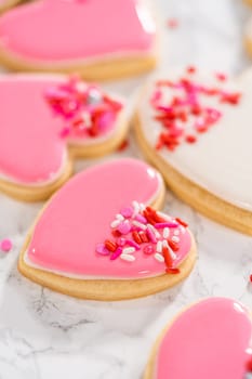 Decorating heart-shaped sugar cookies with pink and white royal icing for Valentine's Day.