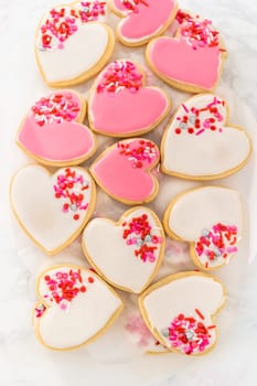 Storing heart-shaped sugar cookies with pink and white royal icing in a large plastic container.