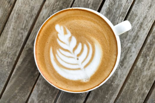 White cup of coffee with pattern on top of foam, against background of wooden table, top view