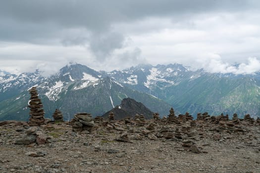 Stacked rock formations create a unique landscape against a backdrop of majestic mountains and cloudy skies. This serene spot showcases nature's beauty and tranquility at elevation.