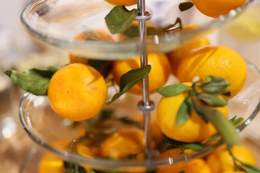 A vibrant display of fresh oranges with green leaves in a glass stand, enhancing any decor with natures touch