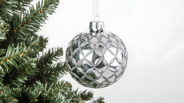 A shiny silver Christmas ornament hanging from a tree branch.
