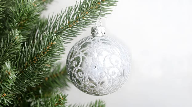 A silver ornament hanging on a Christmas tree branch.