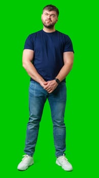 Man standing with a thoughtful expression in a casual outfit against a green background in studio