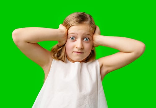 A young girl covers her ears with a worried expression in front of a bright green background in studio