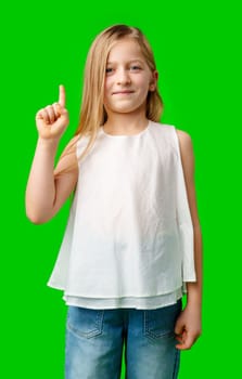 Young girl in casual attire pointing upward against a bright green background in studio
