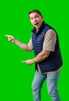 Man in a navy vest gestures enthusiastically toward a green screen in studio