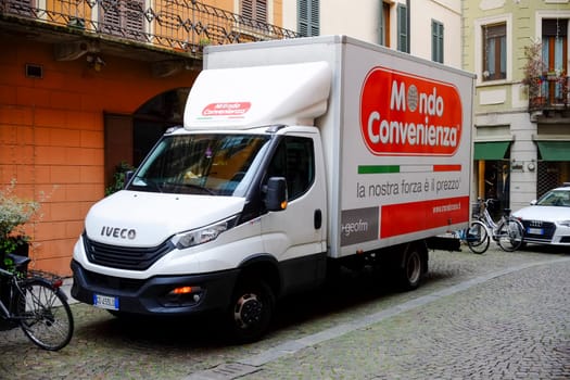 Cremona, Itally - October 6th 2024 Parked white iveco daily truck displaying mondo convenienza advertisement on a cobblestone street in an urban environment