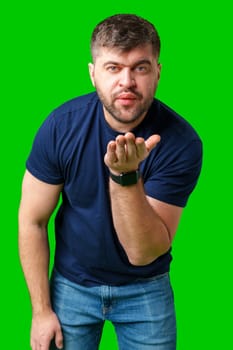 A man blowing a kiss while standing against a bright green backdrop in a casual outfit close up