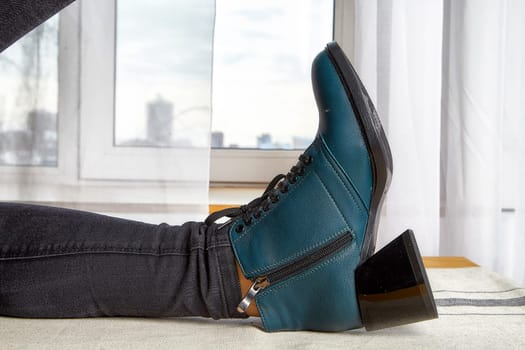 Stylish model poses with one leg elevated, highlighting chic teal ankle boots against an urban backdrop.